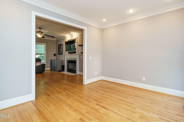 unfurnished living room with crown molding, light wood finished floors, a ceiling fan, baseboards, and a fireplace with flush hearth