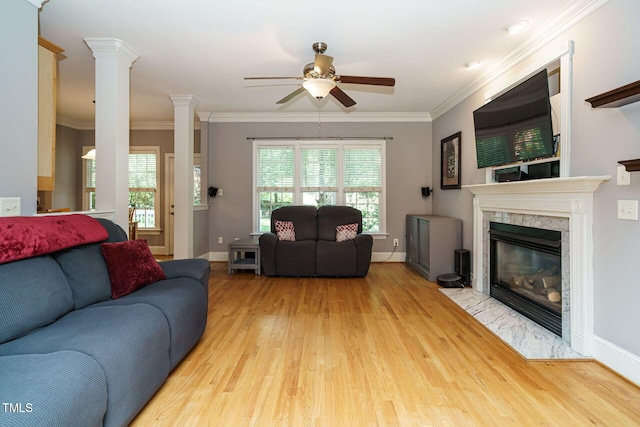 living room with decorative columns, a ceiling fan, a high end fireplace, ornamental molding, and light wood-style flooring