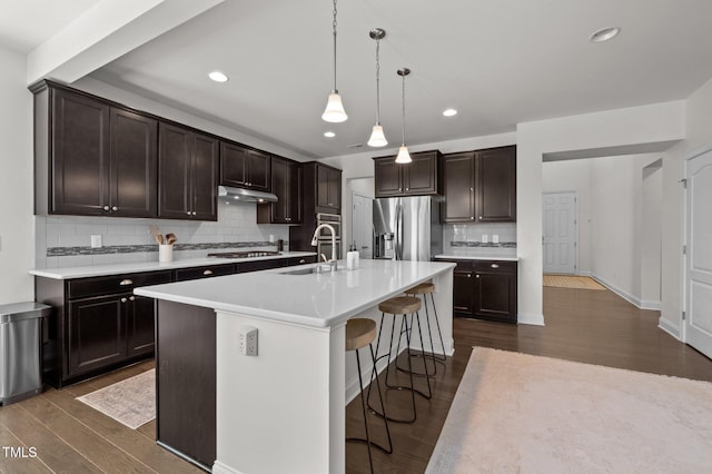 kitchen featuring a breakfast bar area, dark wood-type flooring, under cabinet range hood, appliances with stainless steel finishes, and backsplash