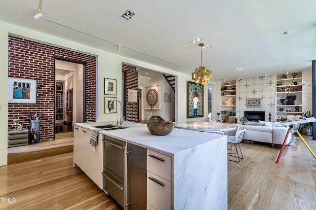 kitchen with light wood-type flooring, a chandelier, a kitchen island with sink, and a sink
