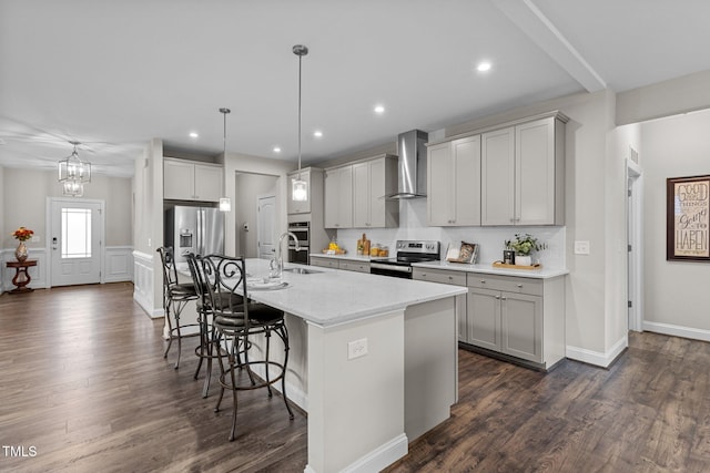 kitchen with a kitchen island with sink, dark wood-style floors, wall chimney range hood, a kitchen bar, and appliances with stainless steel finishes