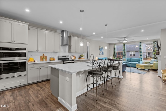 kitchen with a sink, dark wood finished floors, wall chimney exhaust hood, stainless steel appliances, and a kitchen bar