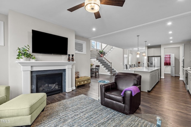 living area with stairs, a glass covered fireplace, recessed lighting, a ceiling fan, and dark wood finished floors
