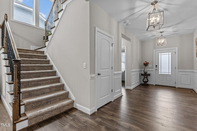 entrance foyer featuring stairway, wainscoting, dark wood finished floors, and a chandelier