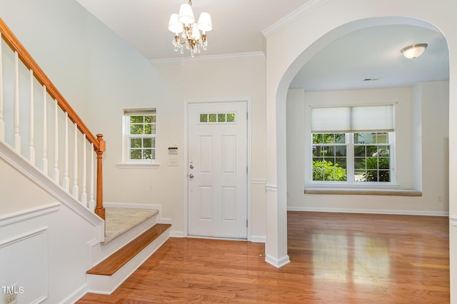 foyer entrance with ornamental molding, light wood-style floors, baseboards, stairway, and arched walkways