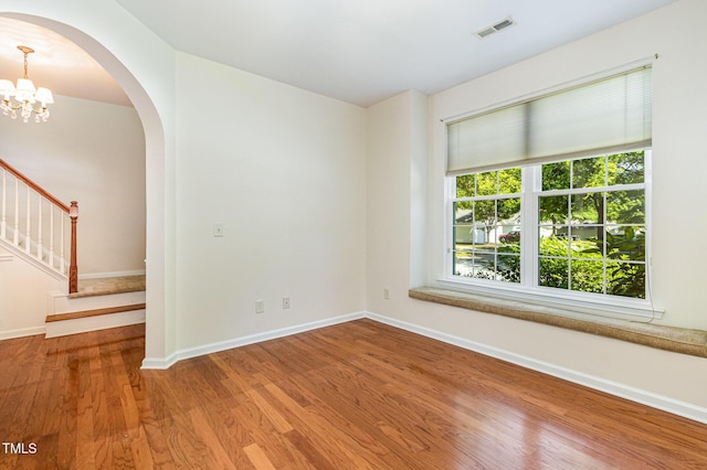 unfurnished room featuring visible vents, arched walkways, wood finished floors, baseboards, and stairs