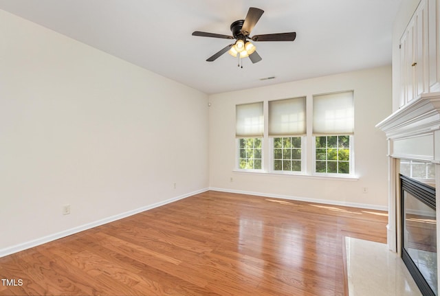 unfurnished living room with a premium fireplace, a ceiling fan, baseboards, and light wood-type flooring