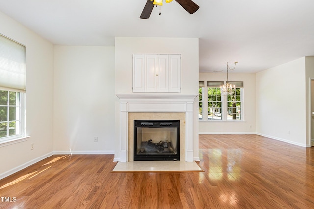 unfurnished living room featuring a fireplace with flush hearth, a healthy amount of sunlight, ceiling fan with notable chandelier, and light wood-style floors