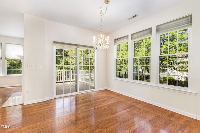 unfurnished dining area with baseboards, a notable chandelier, a healthy amount of sunlight, and wood finished floors