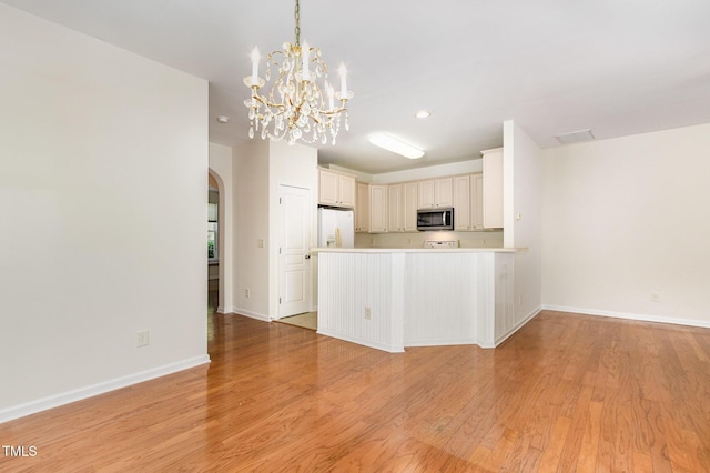 kitchen featuring white refrigerator with ice dispenser, light countertops, stainless steel microwave, arched walkways, and light wood finished floors
