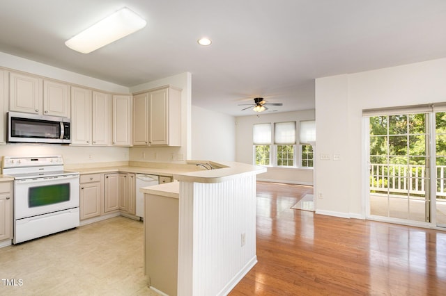kitchen with light countertops, a peninsula, cream cabinetry, and white appliances