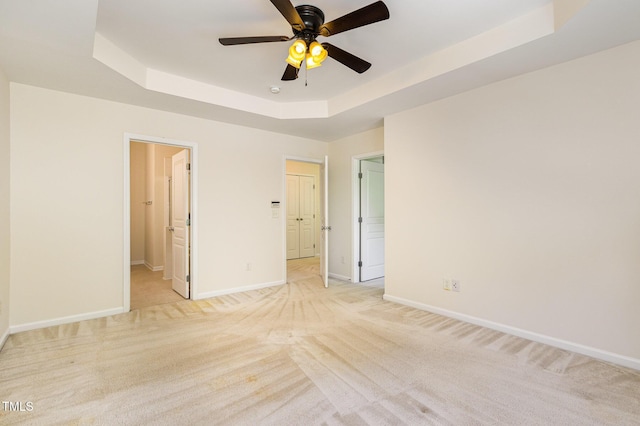 unfurnished bedroom featuring baseboards, light colored carpet, a raised ceiling, and ensuite bath