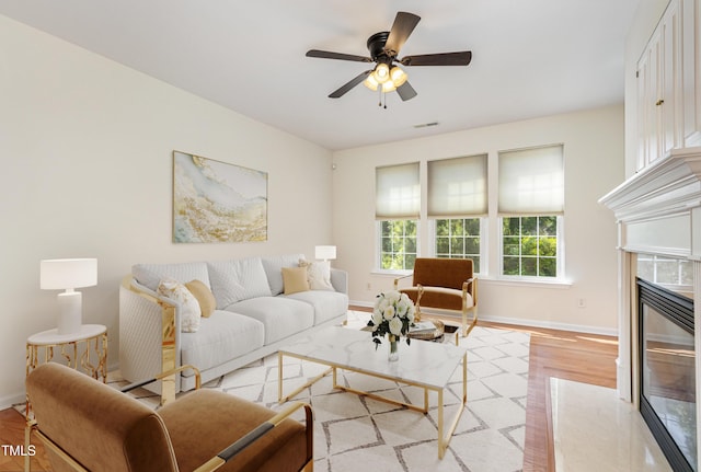 living area featuring baseboards, ceiling fan, and light wood finished floors