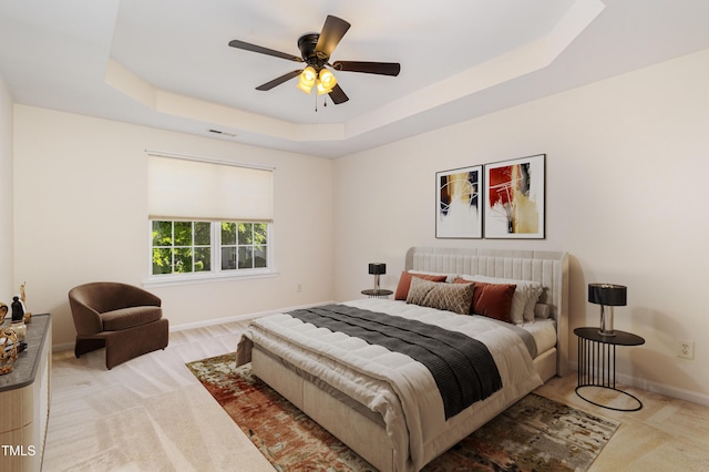 bedroom featuring visible vents, light carpet, baseboards, a tray ceiling, and a ceiling fan