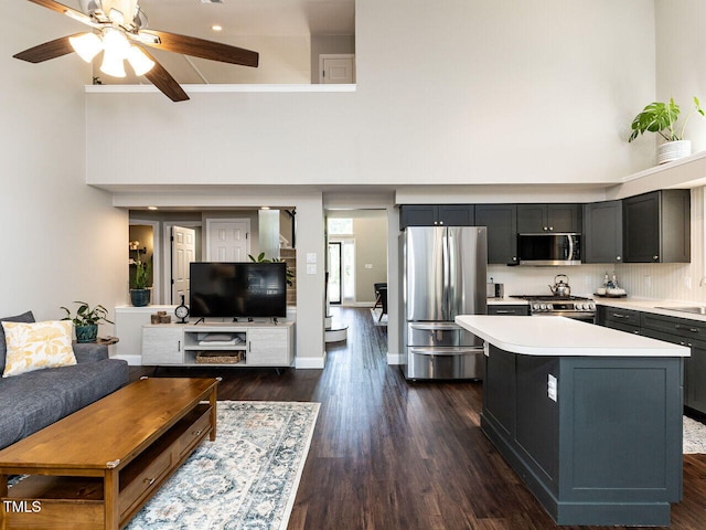 kitchen with appliances with stainless steel finishes, a towering ceiling, light countertops, a center island, and a sink