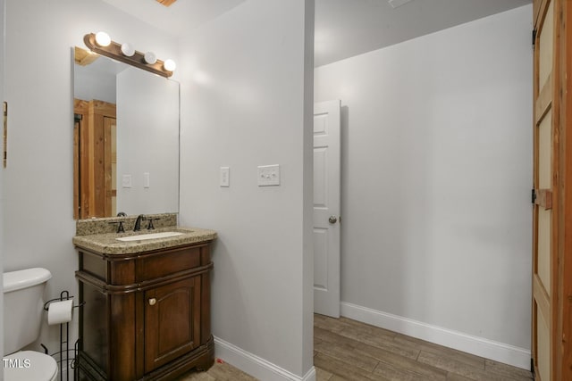 half bath featuring wood finished floors, toilet, baseboards, and vanity