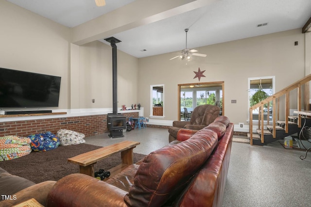 living room with a ceiling fan, a wood stove, speckle patterned floor, and stairs