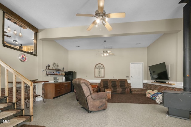 living area featuring ceiling fan, a wood stove, beamed ceiling, stairs, and speckle patterned floor