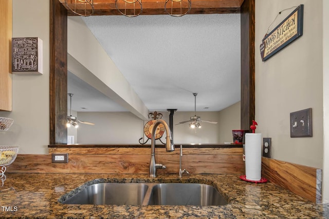 kitchen featuring a sink, ceiling fan, dark stone countertops, and a textured ceiling