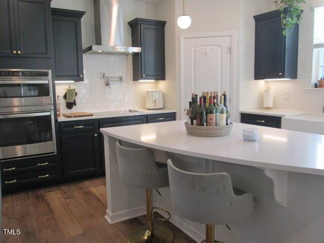 kitchen with a kitchen breakfast bar, stainless steel double oven, wall chimney exhaust hood, electric stovetop, and light countertops