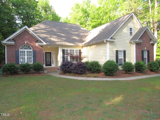 view of front facade with brick siding, a shingled roof, and a front yard