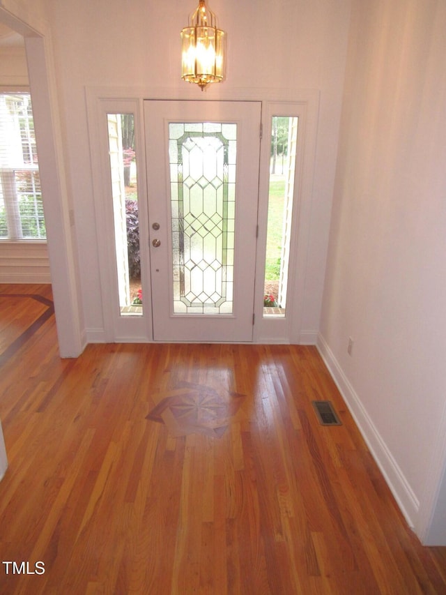 entrance foyer featuring a chandelier, baseboards, a wealth of natural light, light wood-type flooring, and visible vents