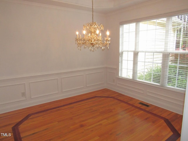 unfurnished dining area with visible vents, crown molding, wainscoting, an inviting chandelier, and a decorative wall