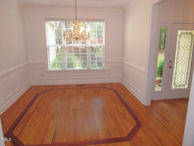 unfurnished dining area featuring a decorative wall, wood finished floors, and a notable chandelier