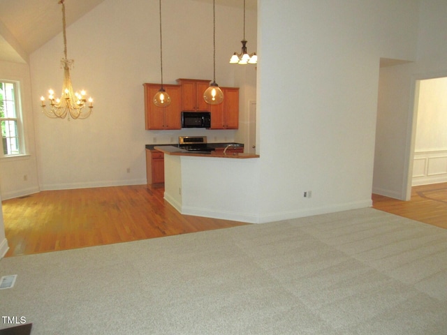 kitchen featuring stainless steel range oven, a notable chandelier, black microwave, and high vaulted ceiling