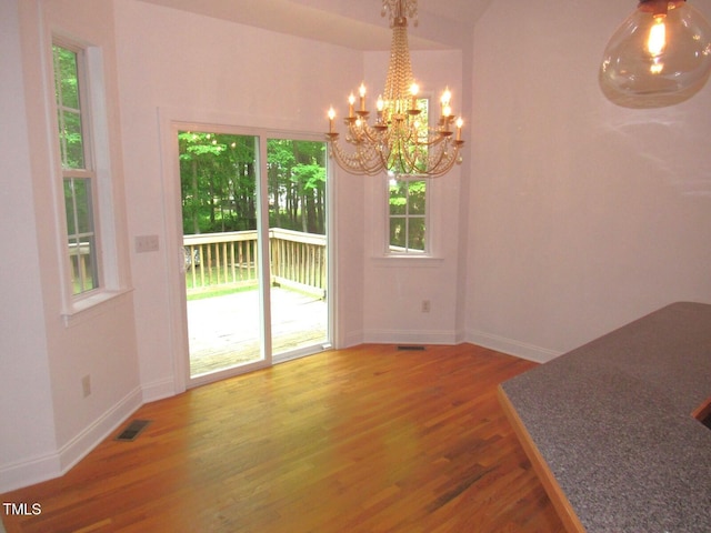 unfurnished dining area featuring a chandelier, baseboards, visible vents, and wood finished floors