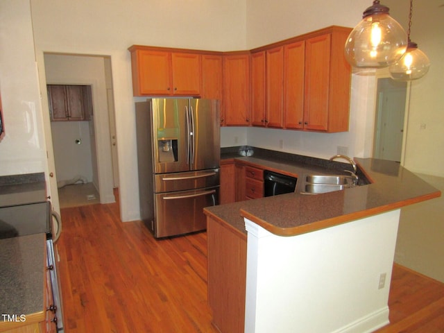 kitchen with a peninsula, dark countertops, stainless steel fridge with ice dispenser, a sink, and light wood finished floors