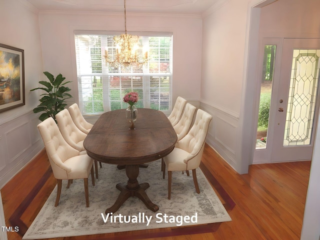 dining area with crown molding, a decorative wall, wood finished floors, and a notable chandelier