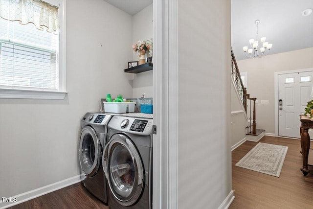 clothes washing area featuring washing machine and clothes dryer, laundry area, a notable chandelier, baseboards, and wood finished floors