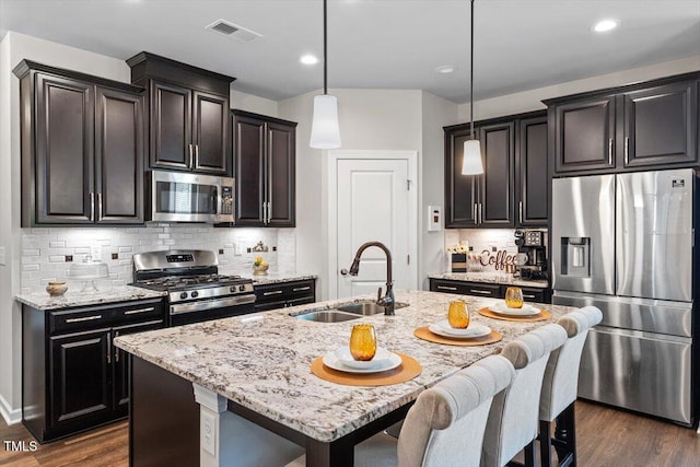 kitchen featuring visible vents, light stone countertops, a center island with sink, a sink, and stainless steel appliances