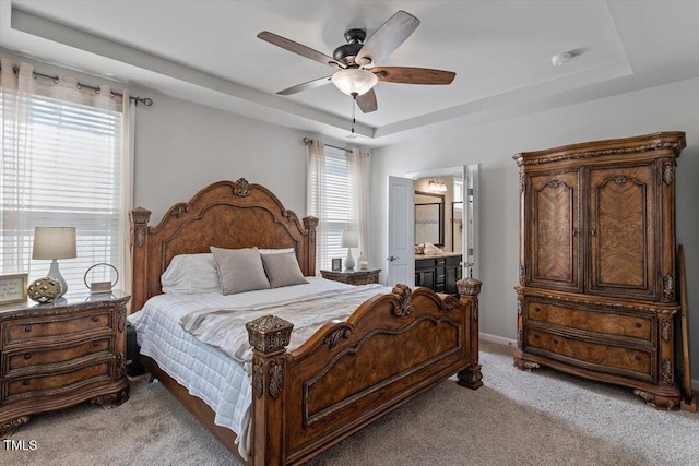 bedroom with ceiling fan, a raised ceiling, baseboards, ensuite bathroom, and light carpet
