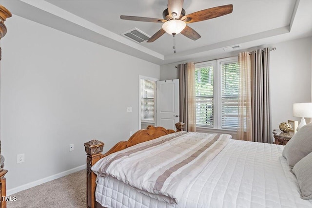 carpeted bedroom with a ceiling fan, a tray ceiling, visible vents, and baseboards