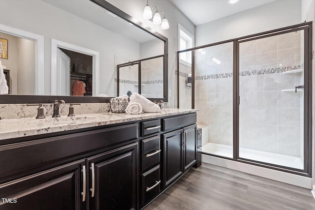 full bath featuring double vanity, a shower stall, a sink, and wood finished floors