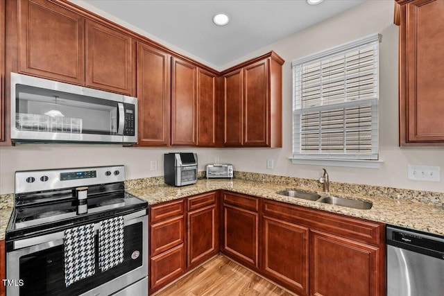 kitchen featuring stainless steel appliances, light stone countertops, a sink, and light wood-type flooring