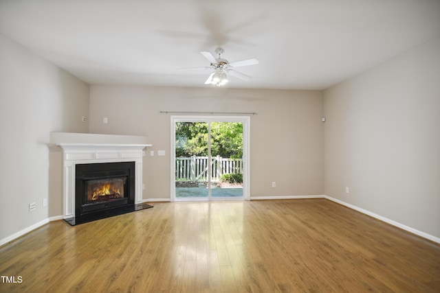 unfurnished living room with a glass covered fireplace, baseboards, ceiling fan, and wood finished floors