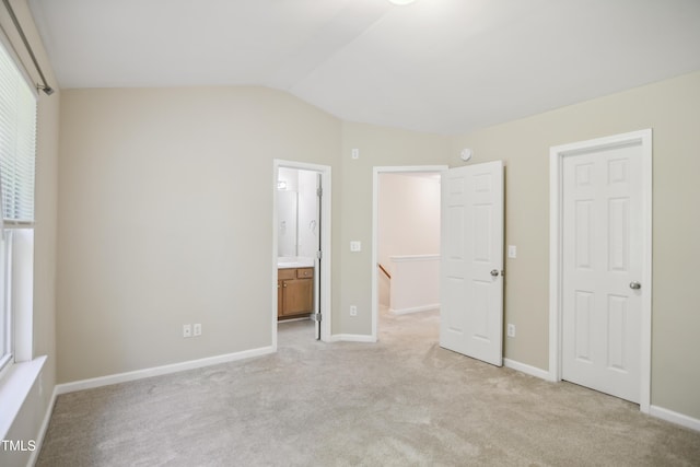 unfurnished bedroom featuring baseboards, ensuite bath, vaulted ceiling, and light carpet