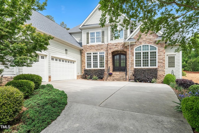 craftsman-style house featuring driveway, french doors, roof with shingles, a garage, and stone siding