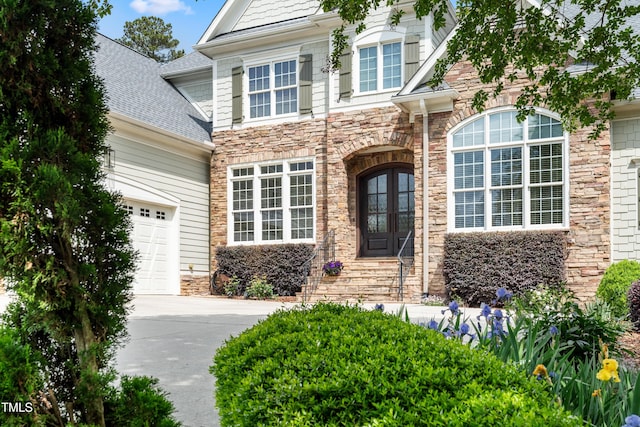 traditional-style home featuring a shingled roof, an attached garage, driveway, and stone siding