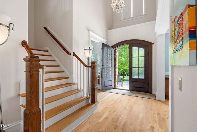 entrance foyer with an inviting chandelier, stairs, a towering ceiling, wood finished floors, and arched walkways