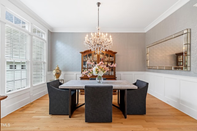dining area featuring an inviting chandelier, ornamental molding, wainscoting, and light wood-style flooring