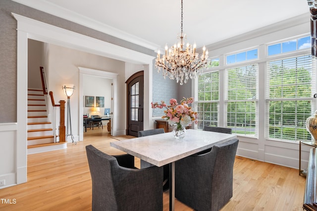 dining room featuring light wood-type flooring, ornamental molding, stairs, and a chandelier