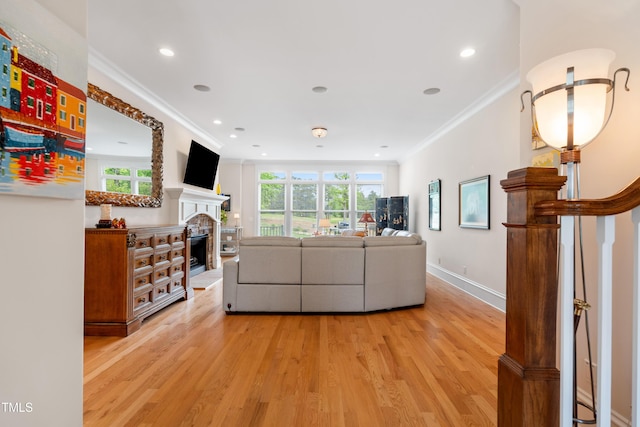 living room with a fireplace with raised hearth, recessed lighting, ornamental molding, and light wood-type flooring