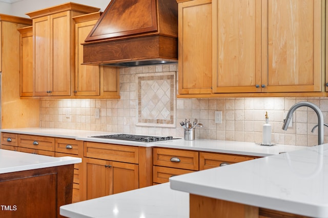 kitchen featuring light countertops, backsplash, custom range hood, and gas stovetop
