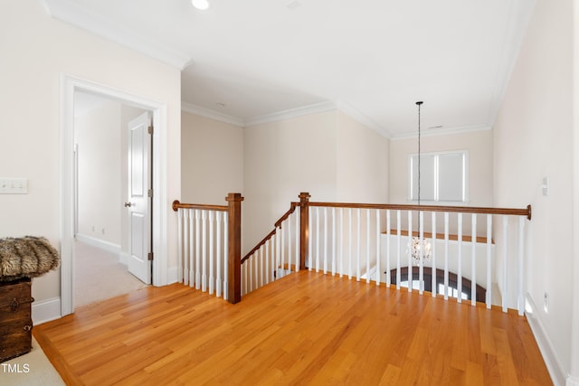 hallway featuring baseboards, ornamental molding, light wood-type flooring, and an upstairs landing