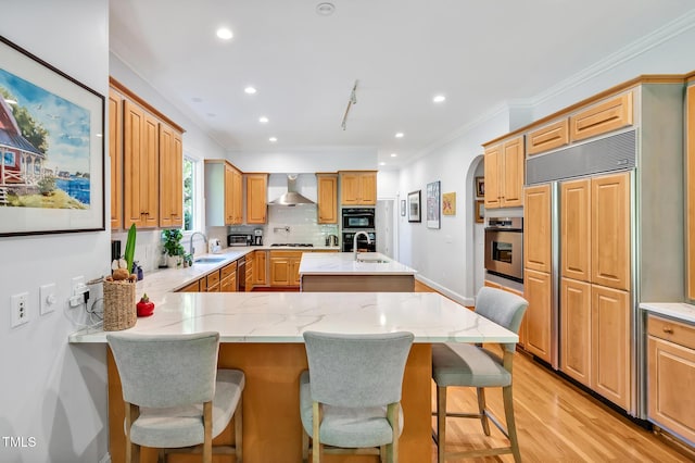 kitchen with wall chimney range hood, a sink, recessed lighting, paneled refrigerator, and light wood-type flooring