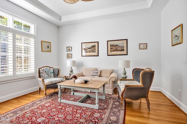 living room with baseboards, ornamental molding, a tray ceiling, and light wood-type flooring